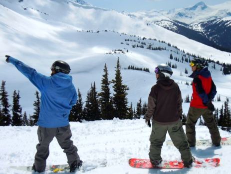 3 boys taking in the view at the top of a snowy peak in Canada whilst pausing for a break on their snowboards