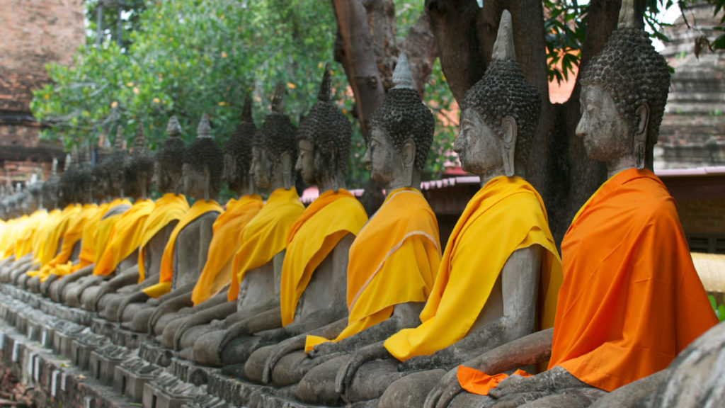 Buddha statues sit in a line at the Ayutthaya temple, dressed in bright orange robes