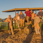 A group of volunteers sit on a game vehicle in the sunset