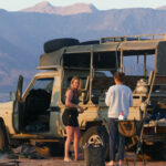 Three girls chat outside the game vehicle with a mountain backdrop