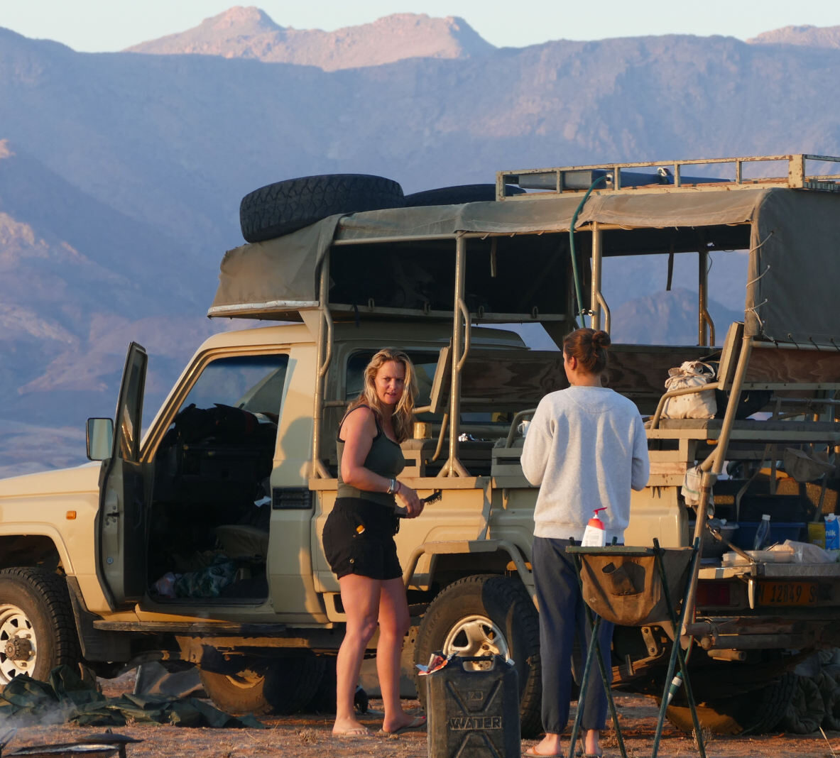 Three girls chat outside the game vehicle with a mountain backdrop
