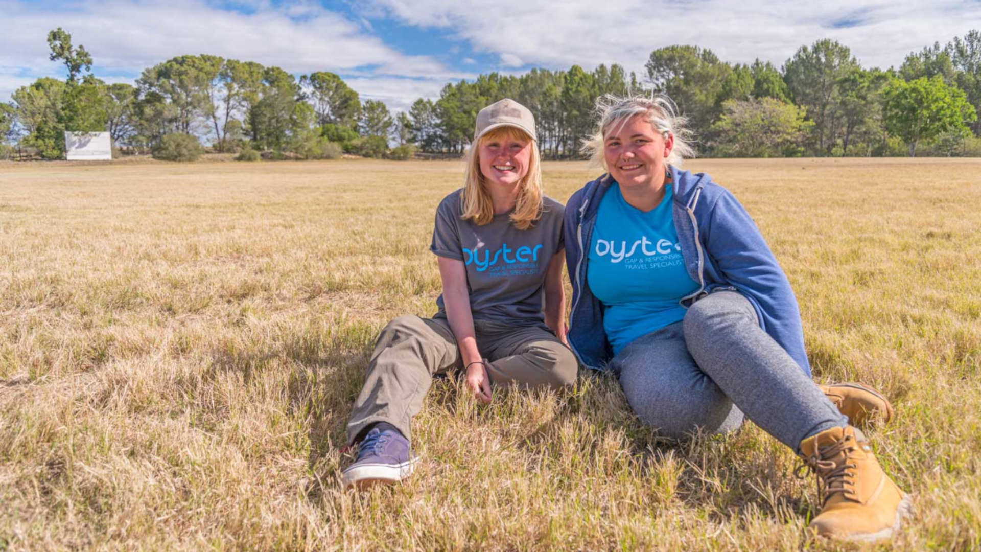 Two volunteers wearing Oyster t shirts sit in the bush facing the camera