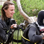 Two divers in their diving gear on land smiling after a successful dive